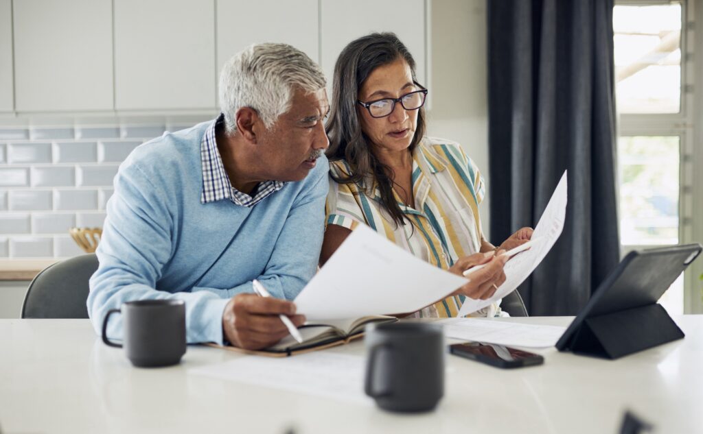 A senior couple reviewing financial documents together at a table, using a tablet.