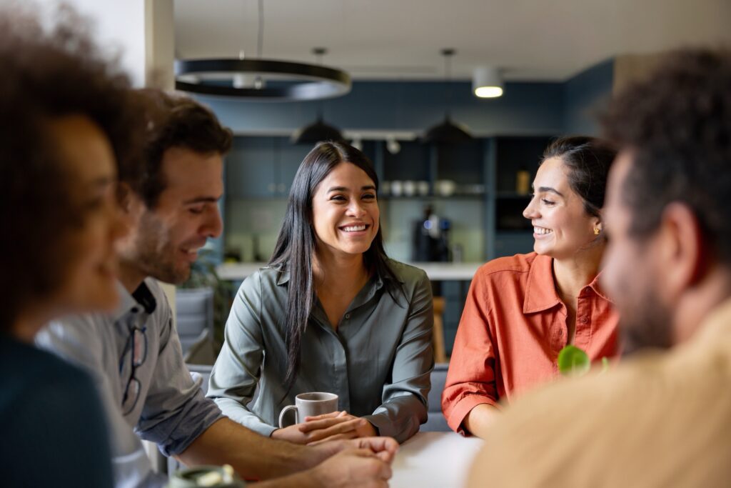 A group of colleagues smiling and having a casual conversation in a modern office setting.