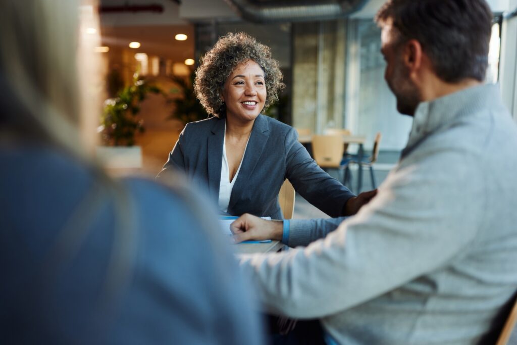 A professional woman smiling and having a conversation with a client in a modern office setting.